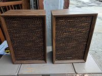 Pair of vintage Pioneer PR 1201 speakers with brown woven grill fabric and wood veneer frames on outdoor table.