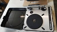 Open Numark PT01 USB portable record player showing black felt platter and tonearm inside hard plastic carrying case.