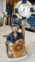 Front view of porcelain sailor clock showing sailor figure holding ship's wheel with clock above.