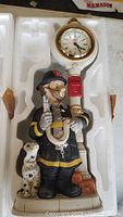 Top-down image of the firefighter clock figurine housed inside the styrofoam mold, showing the clock face, firefighter figure, and Dalmatian dog beside it.