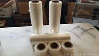 Five rolls of clear shrink wrap plastic film on table including two full-sized and three hand-sized rolls.