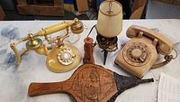 Two vintage rotary dial phones, a small lamp, a wooden bellows and a carved wooden figure on a table