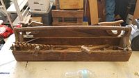 Wooden tool carrier filled with various antique tools including saws, hammers, and auger bits, showing overall condition and contents.