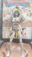Front view of the silver-tone pewter Wonder Woman figure posed with crossed arms holding bracelets above her head, detailed costume and hair visible, with colorful comic-style backdrop.