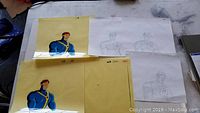 Photo showing two hand-painted animation cels and three pencil sketches of Cyclops from the X-Men cartoon series laid out on a surface.