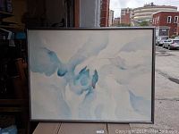 Full view of the large abstract painting on canvas featuring predominantly soft blue and white tones, framed in black.