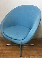 Front view of the vintage blue upholstered swivel chair showing bucket seat and metal swivel base.