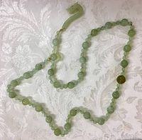Full view of the long jade bead necklace laid out on white textured fabric.