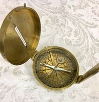 Open brass compass showing detailed dial with degree markings and needle.