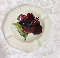 Top-down view of octagonal cream ashtray featuring deep red hibiscus flower and green leaves with glossy finish.