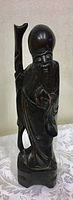 Front-side view of the carved wooden Asian figure showing head, beard, facial features, and staff on back.