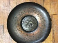 Full view of the metal wall hanging showing circular metal plaque with patinated finish and central embossed medallion with figure.