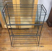 Front view of black metal mid century modern bookrack with three tiers and horizontal rod shelving.