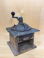 Full view of antique coffee grinder with wooden base and metal top, showing crank handle and embossed lid.