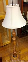 Full view of the maple wood floor lamp showing the turned wood base and white fabric shade on wooden floor inside a room.