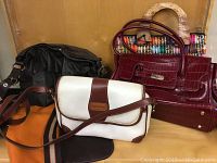 Five purses displayed together: black pleated leather, white and brown crossbody, burgundy crocodile embossed, multicolor woven with wooden handles