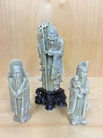 Front view of all three stone figurines together on a wooden surface