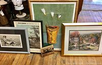 Five framed art prints arranged on a wooden floor showing all items together, including various styles and subjects