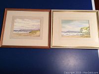 Two framed coastal watercolour paintings laid on blue surface, showing the overall lot condition and framing.