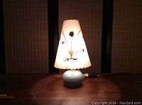 Lamp illuminated on wooden surface showing blue pottery base and lighted floral shade.
