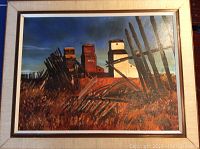 Framed oil painting of three grain elevators with dry wheat foreground under dark blue sky.