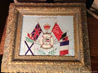 Full view of framed embroidered fabric panel featuring Allied victory flags with ornate gold frame and glass cover.