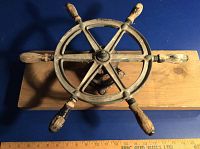 Top down view of the steering wheel mounted on pine board showing six wooden handles and metal wheel.