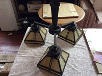 Three-arm ceiling light fixture with stained glass panels resting on lace tablecloth showing the overall style and lampshades.