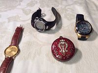 Four watches on white cloth: gold analog, black digital, analog-digital, red enamel pocket watch
