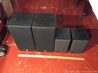 Two sets of speakers side by side on red floor, one larger pair marked JBL and one smaller pair marked TAEYERS, with ruler for scale.