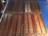 Four pairs of antique wooden window shutter panels laid out on a flat surface showing their aged wood and metal hardware
