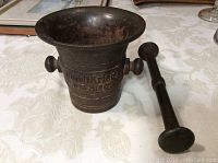 Angled view of the cast iron mortar and pestle showing inscription and handles on mortar.