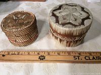 Top view of two round Indigenous quill boxes with ruler showing sizes, quillwork design visible
