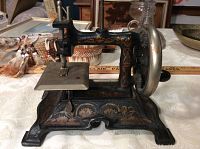Front side view of the antique cast iron sewing machine showing hand crank, sewing platform and painted designs.