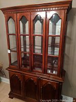 Front view of mahogany hutch showing glass doors on upper cabinet and wood doors on lower cabinet with decorative handles and molding details.