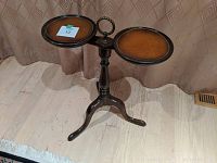 Photo of a small wooden curio table with two round tabletops and a central ring handle, supported by a tripod base with three curved legs.