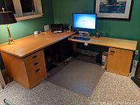 L-shaped desk and credenza in a home office setting, showing desk with three drawers and credenza with storage door, lamp and computer monitor on top, carpeted floor.