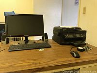 Photo of Samsung monitor, Isus keyboard and mouse, two speakers, Epson WF2540 printer on wooden table.