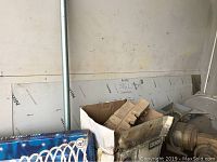 Partial polished stainless steel sheet leaning against a wall with protective film markings and handwritten '316L 14 ga' note visible. Also visible are boxes and other materials placed nearby.