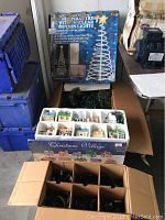 Boxed six-foot tall spiral Christmas tree light with clear motion lights pictured upright next to Christmas village box and blue crates.