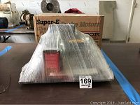 Front view of Baldor motor shrink wrapped with packaging box behind it and MaxSold lot tag.