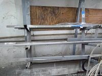 Long horizontal metal tubes of various types and diameters arranged on a metal rack against a wall, showing stainless steel and aluminum tubing.