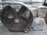 Full front view of the large industrial fan with black grille and smaller sitting fan next to it