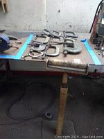 Top view of various sized metal C-clamps and metal roller on wooden table