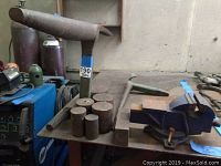 Overview of bench vise, green stake stand and assorted metal pieces on table