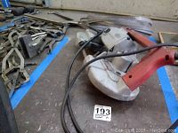Full view of Milwaukee electric bandsaw with red handle lying on surface with other tools around.
