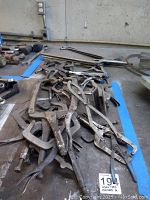 Various metal clamps piled together on a workshop bench, showing different types and sizes, including locking pliers clamps and C-clamps.