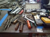 Wide view of assorted hand tools including pliers, wire strippers, screwdrivers, wrenches, and measuring tapes on a table.