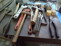 Photo showing multiple crescent wrenches, mallets with wooden heads, and other hand tools on a surface.