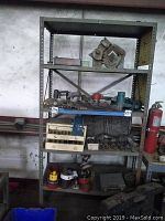 Metal shelf with assorted tools and accessories on two shelves arranged in workshop environment.